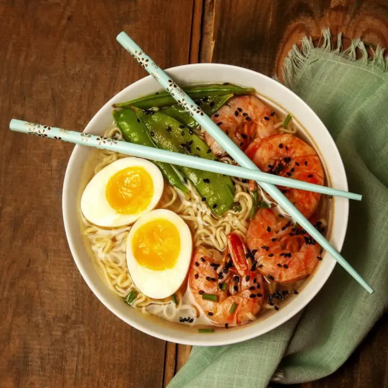A bowl of ramen with soft-boiled eggs, shrimp and snow peas